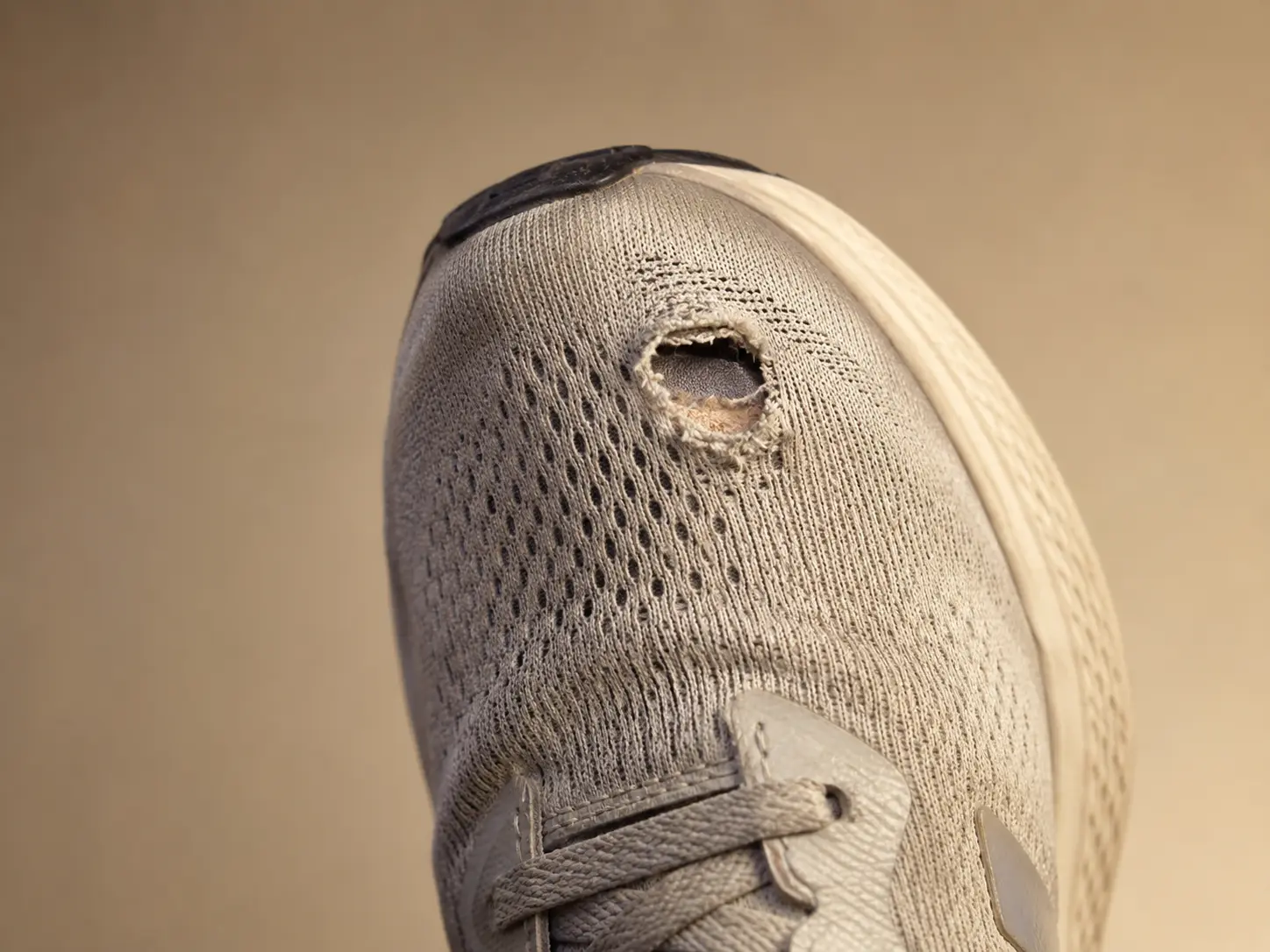 Close-up of a worn sneaker with a hole in the mesh fabric above the big toe area