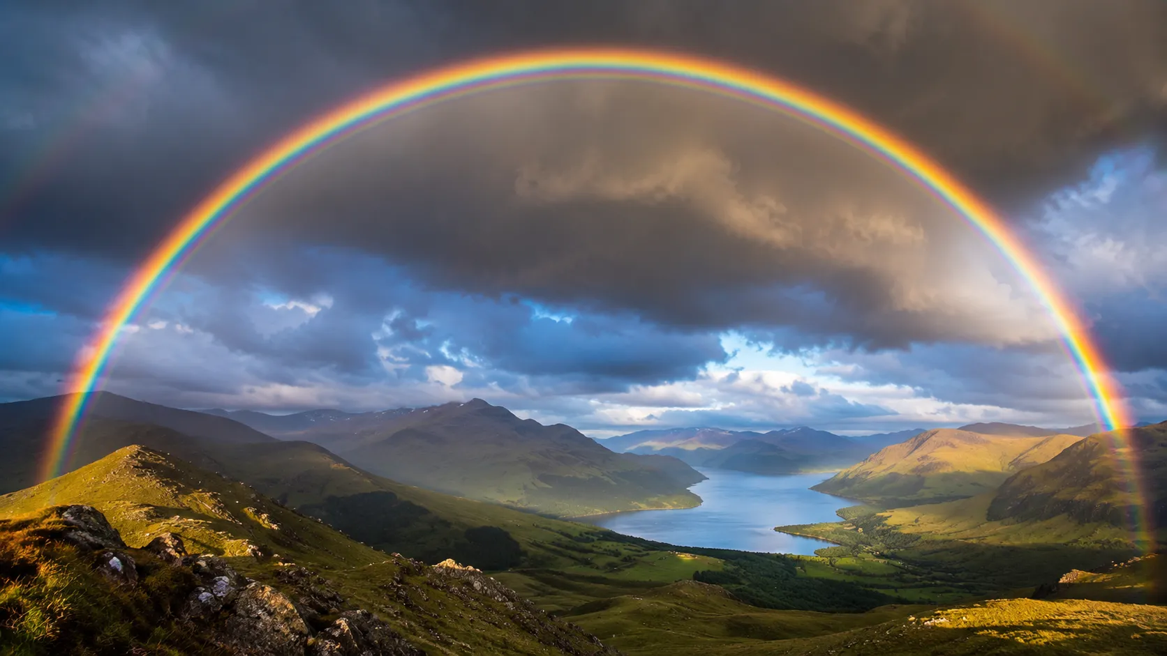 Full rainbow arc over an open green field after rain