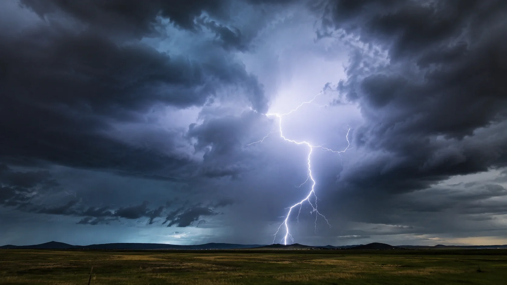 Lightning strike illuminating dark storm clouds over a flat landscape